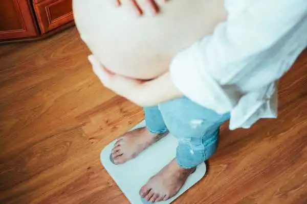 Image of woman weighing herself and experiencing weight gain through pregnancy East Retford